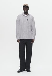 Striped button-up shirt in gray and white, paired with black trousers, and dark shoes. A beige cap complements the outfit.