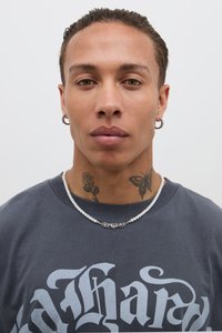 Modelo a vestir uma t-shirt cinza com grandes letras brancas, um colar de pérolas com detalhes em prata e tatuagens visíveis de uma rosa e uma borboleta.