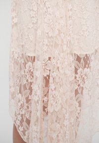 Peeneline kangas pehmeas roosakas värvitoonis, millel on lillemustrid ja läbipaistev tekstuur, elegantsetena langeb, kusjuures sisekiht on osaliselt nähtav.