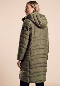 Oliwkowa kurtka puffer z kapturem, posiadająca pikowaną strukturę, długie rękawy oraz okrągły detal z logo na lewym rękawie.
