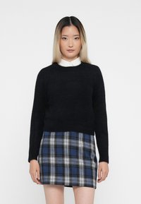 Schwarzer, flauschiger Pullover mit langen Ärmeln, kombiniert mit einem karierten Minirock in Blau und Schwarz, der weiße Akzente aufweist. Ein einfacher Kragen ist unter dem Pullover sichtbar.