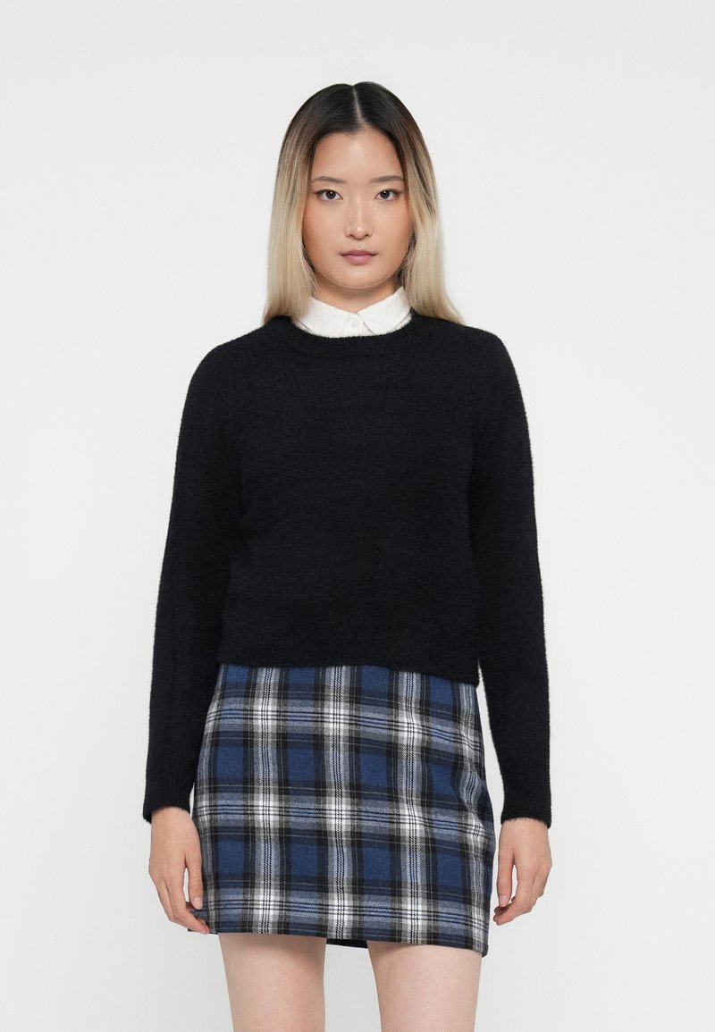 Schwarzer, flauschiger Pullover mit langen Ärmeln, kombiniert mit einem karierten Minirock in Blau und Schwarz, der weiße Akzente aufweist. Ein einfacher Kragen ist unter dem Pullover sichtbar.