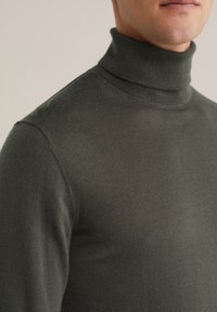 Mörkgrön turtleneck-tröja av mjukt, stickat tyg. Har en hög halsringning och en figurnära design, perfekt för lager-på-lager.