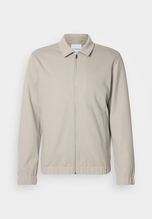 Jasnobeżowa kurtka zapinana na zamek z kołnierzykiem, elastycznymi mankietami i bocznymi kieszeniami. Wykonana z miękkiego, gładkiego materiału.