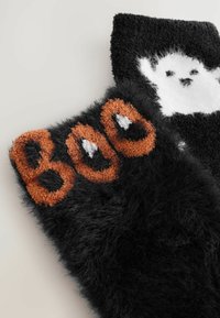 Soft black fuzzy socks with orange "BOO" text on one and a white ghost design on the other, set against a light background.