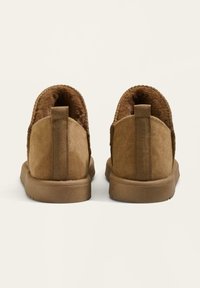 Hnědé semišové kotníkové boty s měkkou kožešinovou podšívkou, poutkem na zadní straně a texturovanou gumovou podešví pro lepší trakci.