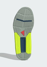 Suela gris con brillantes acentos amarillos y un patrón de agarre texturizado. Presenta una sección del mediopié de color azul y un logo rojo cerca del talón.