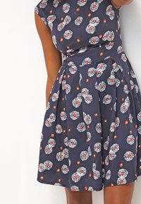 Tmavě modré bavlněné šaty se přiléhavým živůtkem a skládáním sukně, s květinovým vzorem v bílé, červené a černé barvě. Součástí jsou krátké rukávy.