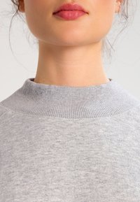 Sudadera gris texturizada con un alto cuello de canalé. La tela parece suave y casual, con un sutil patrón jaspeado.