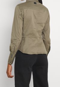 Olivgrön jacka med åtsittande midja, knappade ärmslut och en detalj i bakseam. Gjord av ett lättviktigt material har den en ren design.