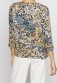 Blomsterbluse i sort med blå, gul og hvide mønstre. Den har en løstsiddende pasform, trekvartærmer og en buet kant.