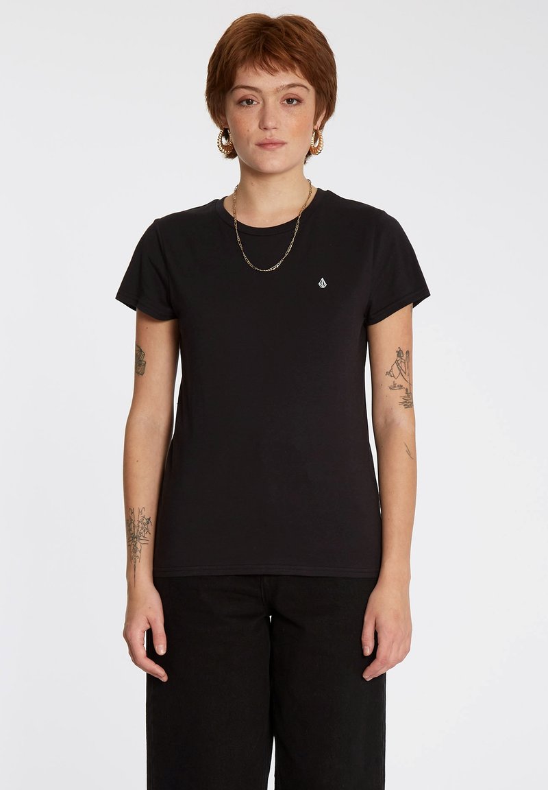 Zwarte katoenen t-shirt met korte mouwen, ronde halslijn en klein logo op de linkerborst. Gecombineerd met high-waisted zwarte broek.