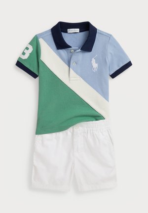 Camisa polo en azul, verde y blanco con mangas cortas, 3 apliques en la manga izquierda; combinada con pantalones cortos de cintura elástica blanca.