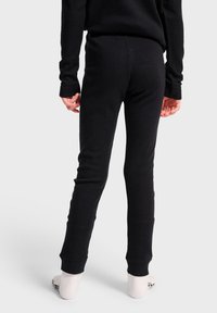 Svarta bomullstights med en figurnära design, avslutade med avsmalnande ben och ribbade cuffar. Baksidan har en slät yta utan synliga mönster.