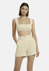 Crème gekleurde crop top met vierkante halslijn, gecombineerd met high-waisted shorts met riemlussen en een knoopsluiting.