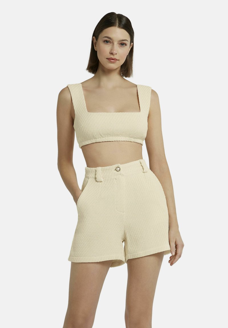 Crème gekleurde crop top met vierkante halslijn, gecombineerd met high-waisted shorts met riemlussen en een knoopsluiting.