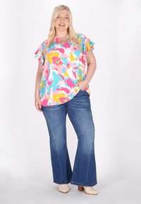 Farverig bluse med abstrakte mønstre og rynkede ærmer, parret med jeans med klokkeformet skæring. Outfitet indeholder nuancer af blå, pink, gul og hvid.