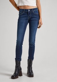 Mörkblå skinny jeans med en lätt stretch, med en medelhög midja, fem fickor och synlig sömnad. Kombineras med svarta klackstövlar.