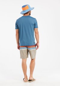 Hellblaues Kurzarmhemd mit strukturiertem Muster, kombiniert mit mehrfarbigen Badeshorts mit horizontalen Streifen und kariertem Design sowie einem geschichteten Hut.