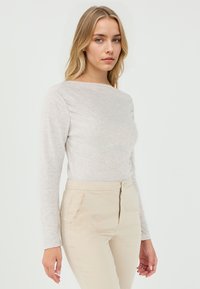 Lichtbeige langemouwtop gemaakt van een zachte stof, met een bootnek en een gladde textuur, gecombineerd met beige broeken en een ritssluiting aan de voorkant.