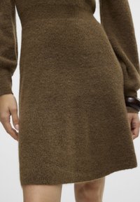 Abito in maglia di un ricco colore marrone, con una morbida e pelosa texture e maniche lunghe, che arriva a metà coscia con un orlo leggermente svasato.