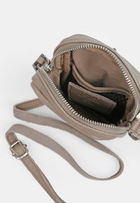 Liten beigefärgad lädercrossbody-väska med en silvrig dragkedja, tygfoder och justerbar rem. Har inre fickor och en mjuk yta.