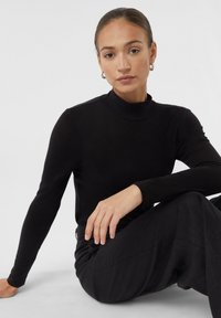 Zwarte lange mouwen turtleneck top gemaakt van een gladde stof, met een aansluitend ontwerp en een zachte textuur, in combinatie met losse zwarte broeken.
