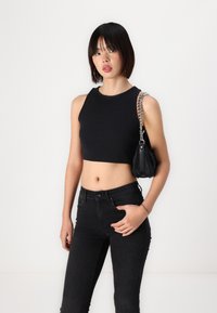 Must musta tank top ümarate kaelustega, täiendanud kõrge vöökohaga mustade teksadega. Mudel kannab väikest musta kotti, millel on hõbedane kett.