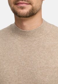 Maglione beige a maglia con scollo rotondo, realizzato in un tessuto morbido e testurizzato con polsini a coste. Vista ravvicinata che mette in evidenza lo scollo e la parte superiore del petto.