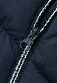 Primer plano de la cremallera de una chaqueta oscura, con un tirador de cremallera negro y costuras blancas junto a la cremallera, destacando la textura de la tela.