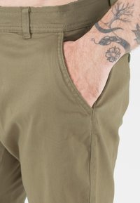 Kakifärgade byxor med en jämn textur, sidoficka och prydligt sydda sömmar. Midjebandet har en enkel design för en säker passform.