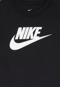T-shirt nera in cotone con un grande logo "NIKE" bianco e l'iconico swoosh. Design semplice con collo a giro e cuciture pulite.