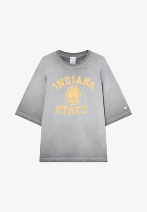 T-shirt grigia over-size con il testo e l'emblema giallo "INDIANA STATE" stampati sul davanti e un piccolo logo sulla manica sinistra.