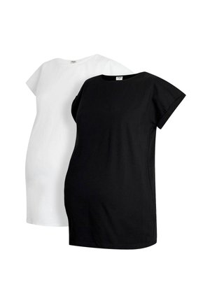 Frau mit blondem Haar, die ein weißes T-Shirt und blaue Jeans trägt, lächelt mit geschlossenen Augen und lehnt mit einer erhobenen Hand an einer weißen Wand.