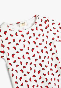 Camiseta blanca de los niños con ribetes, que presenta un patrón repetido de rodajas de sandía en rojo y verde. Cuello redondo y mangas cortas.