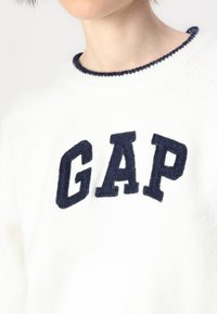 Valge kudumisjärgiga sviiter tumesinise "GAP" logoga. Omab ribatud kaelust kontrastse tumeda äärega. Pehme tekstuur.