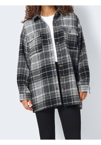 Czarna i szara flanelowa koszula w kratę z dwoma kieszeniami na piersi i złotymi guzikami, o luźnym kroju i długich rękawach. Miękka tekstura.