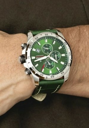 Montre verte au poignet avec un boîtier en acier inoxydable, un bracelet texturé en cuir vert, trois sous-cadrans, et des accents blancs et rouges.