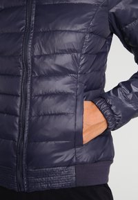 Navy pufferjacka med quiltad design, dragkedja fram, elastiska manschetter och texturerad nederkant. Inkluderar sidofickor för förvaring.