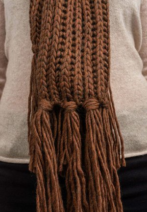 Braun gestrickter Schal aus dickem, strukturiertem Garn. Besitzt geflochtene Enden mit langen Quasten. Wird über einem leichten Pullover getragen.