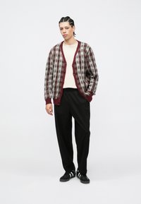 Cardigan en maille marl à carreaux bordeaux et gris avec un col côtelé, doté de boutons sur le devant, assorti à un pantalon noir et des baskets.