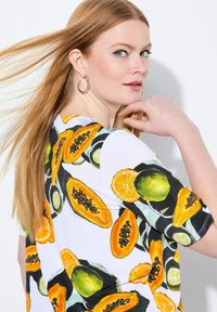 Top floral con un fondo blanco y vibrantes ilustraciones en amarillo y verde de papaya y lima; mangas cortas, tejido suave.