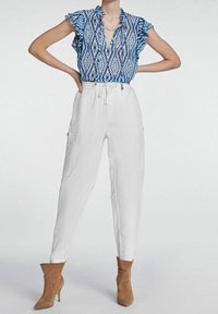 Blouse à motifs bleus et blancs avec manches à volants, associée à un pantalon cargo blanc. Complété par des bottines marron clair. Tenue décontractée.