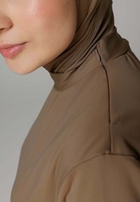 Bruine, strakke zwemkleding met een hoge hals en ritsdetail. Glad textuur, minimalistisch ontwerp en subtiele glans.