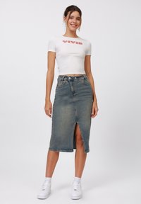 Jupe midi en denim avec une fente à l'avant, délavage bleu clair, taille haute et design classique à cinq poches. Associée à un t-shirt cropped blanc.