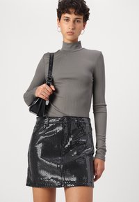 Grijze geribbelde coltrui gecombineerd met een zwarte pailletten minirok. De outfit bevat een kleine zwarte tas met een schouderband en ringoorbellen.