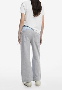 Pantalon de survêtement gris à jambes larges avec une texture douce, doté d'une ceinture élastique bleu clair et de deux poches arrière. Associé à un t-shirt blanc.