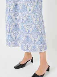 Rochie albă din in cu broderie florală albastră, tiv ondulat, asociată cu mules negre cu toc bloc din patent.