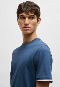 Blå t-shirt med kort ärm och rundad halsringning, med randiga detaljer på ärmarna, tillverkad av ett mjukt och lätt tyg.