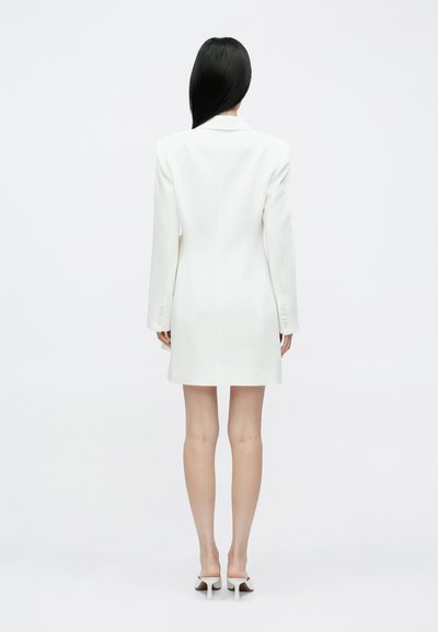 Vestido blazer branco com corte ajustado, mangas compridas e uma abertura única nas costas. Textura suave com design minimalista, sem adornos.